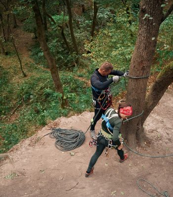 Top view. Man and woman doing climbing in forest with use of safety equipment.
